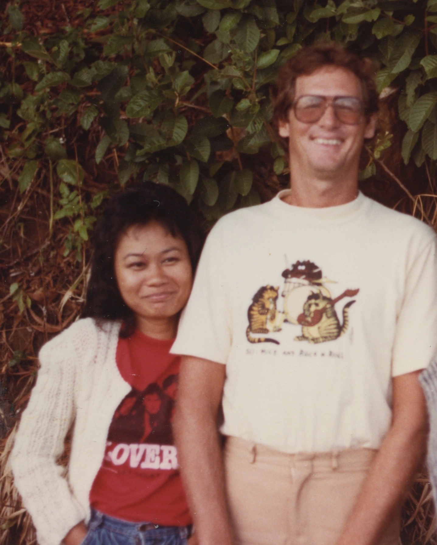 Phil Bennett and his partner wearing floral leis, smiling together at a warm celebration or luau event