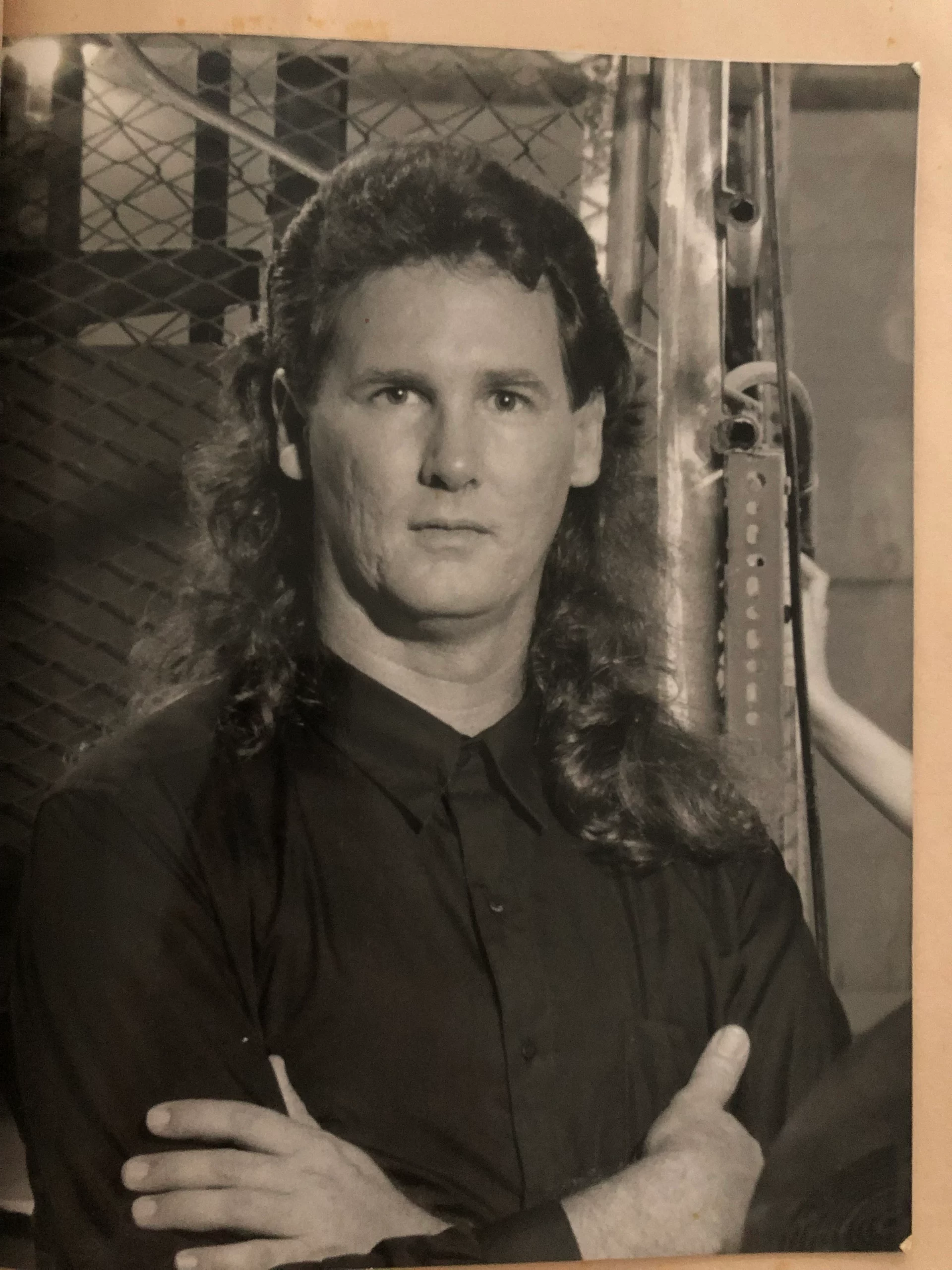 A young Phil Bennett smiling in an orange Club Mediterranee t-shirt with curly hair and glasses in a casual indoor setting